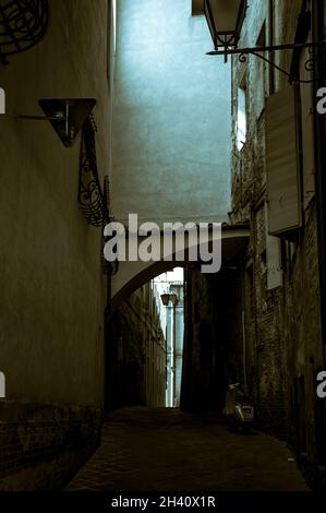 Ruelle sombre étroite et fendue entre les maisons en Italie avec une mobylette, moto garée sur la droite Banque D'Images