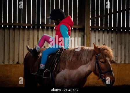 Une jeune fille qui fait « autour du monde » pour tourner en selle pendant des leçons d'équitation dans une arène équestre Banque D'Images