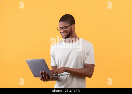 Carrière de freelance.Homme américain africain positif utilisant un ordinateur portable et souriant, debout sur fond jaune Banque D'Images