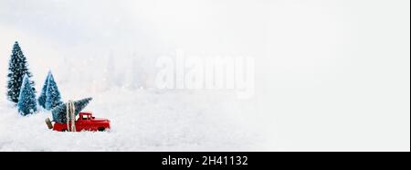 Bannière d'un camion rouge antique des années 1950 transportant un arbre de Noël à la maison à travers une terre d'émerveillement hivernale enneigée.Mise au point sélective sur le véhicule. Banque D'Images