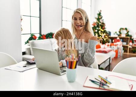 Mère de fille caucasienne portant un micro-casque d'agent de centre d'appels chez elle, pointant le pouce vers le côté souriant heureux avec une bouche ouverte Banque D'Images