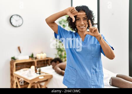 Jeune femme thérapeute au centre de bien-être spa souriant faisant cadre avec les mains et les doigts avec le visage heureux. Créativité et concept de photographie. Banque D'Images