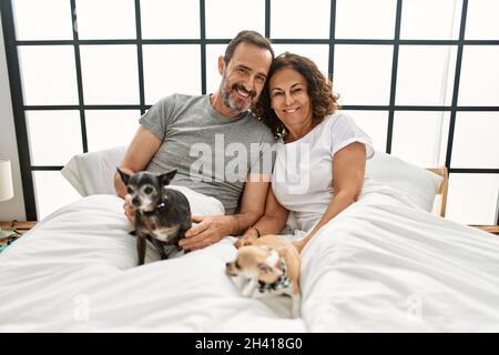 Couple hispanique d'âge moyen souriant heureux couché sur le lit avec des chiens à la maison. Banque D'Images