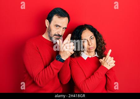 Couple d'âge moyen de femme et d'homme hispanique qui s'embrasse et se tient ensemble tenant une arme symbolique avec un geste de main, jouant tuant des armes de tir, an Banque D'Images