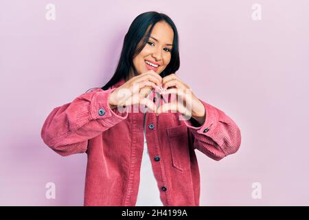 Belle femme hispanique avec piercing de nez portant décontracté veste rose souriant dans l'amour faisant le symbole de coeur forme avec les mains. Concept romantique. Banque D'Images