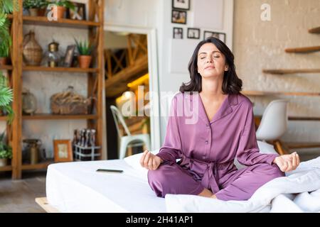 Concept de santé mentale et de détox numérique.Photo d'une femme d'âge moyen méditant au lit. Banque D'Images