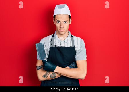 Jeune homme hispanique portant un tablier professionnel tenant le couteau dans le visage de choc, regardant sceptique et sarcastique, surpris par la bouche ouverte Banque D'Images