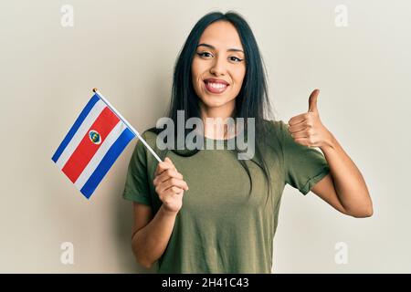 Jeune fille hispanique portant le drapeau du costa rica souriant heureux et positif, pouce vers le haut faisant excellent et signe d'approbation Banque D'Images