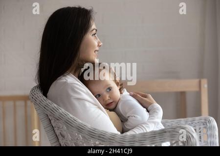 Profil de la mère souriante embrassant la petite fille, assise sur une chaise Banque D'Images