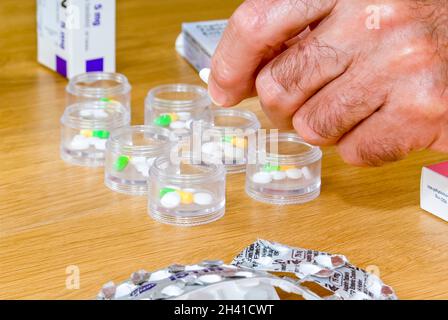 Gros plan horizontal d'un homme âgé organisant ses médicaments hebdomadaires dans des conteneurs individuels, faisant partie d'une tour de stockage. Banque D'Images