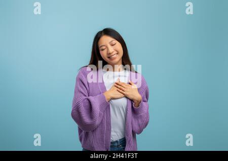 Concept de gratitude.Une femme asiatique reconnaissante, qui garde les deux mains sur la poitrine, exprime son appréciation et sa gentillesse Banque D'Images