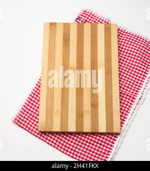 Une planche à découper rectangulaire en bois vide et une serviette rouge dans une cage blanche sur une table blanche, vue du dessus Banque D'Images