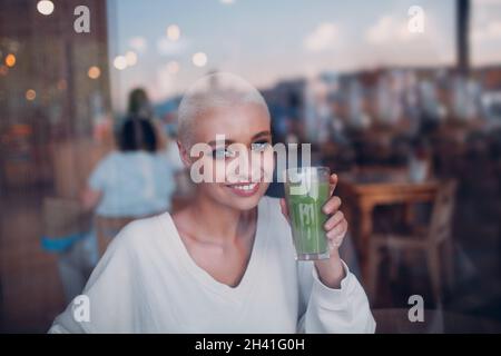 Jeune femme blonde millénial cheveux courts intérieur avec smoothie vert Banque D'Images