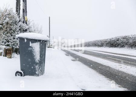 Une poubelle à roulettes, assise sur le côté de la route, dans un paysage enneigé, attendant la collecte hebdomadaire Banque D'Images