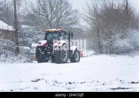 Woodbridge Suffolk Royaume-Uni février 07 2021 : un tracteur rouge stationné en bordure d'un champ de ferme dans un blizzard lourd dans la campagne britannique Banque D'Images