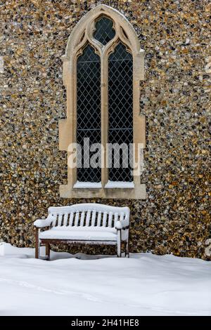 Un banc en bois recouvert de neige à l'extérieur sous une grande fenêtre de l'église Lancet Banque D'Images