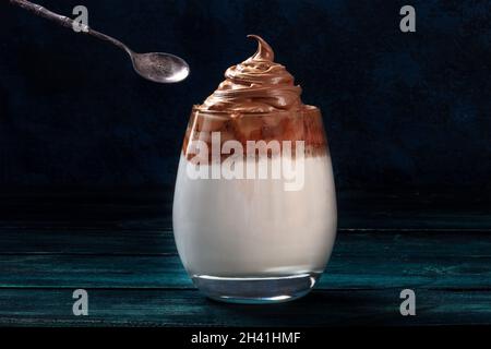 Dalgona café froid dans un verre avec une cuillère, sur fond sombre Banque D'Images