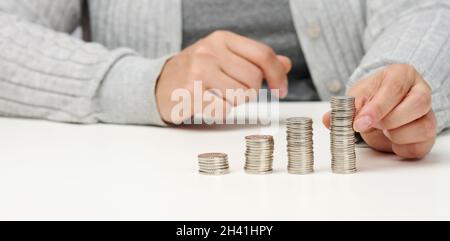 La femme est assise à la table et une pile de pièces de monnaie sur la table.Calcul des dépenses et du revenu, subvention, impôt Banque D'Images