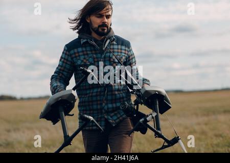 Man pilot holding quadcopter drone in hands at outside field. Stock Photo