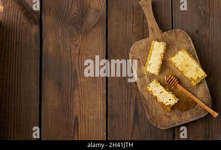 Une pile de chelines de cire avec du miel sur une planche en bois et une cuillère en bois, table brune Banque D'Images