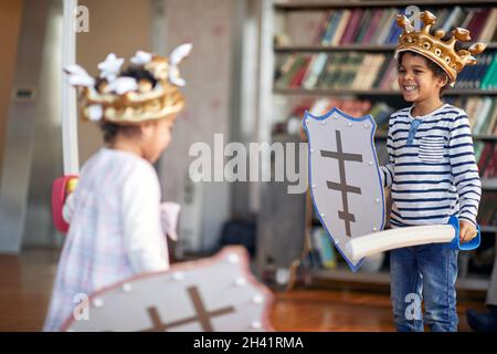 Un petit frère et une sœur habillés comme des chevaliers sont prêts pour le jeu de combat d'épées tout en jouant dans une atmosphère gaie à la maison.Famille, maison, playtim Banque D'Images