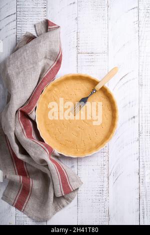 Pâte à cuire quiche, tarte ou tarte en céramique prêt à cuire sur une serviette de cuisine sur fond blanc en bois de planche rustique ancien. Vue de dessus, c Banque D'Images