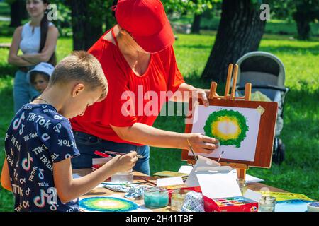 Zaporizhia, Ukraine- 19 juin 2021: Fête de la famille de charité: Femme – volontaire expliquant à un garçon comment peindre l'image avec des peintures à l'aquarelle à Banque D'Images