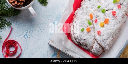 Wholegrain Stollen aux raisins secs et sucre en poudre sur une serviette en lin avec un tamis, ruban rouge sur le fond bleu clair de béton enneigé.Tradition Banque D'Images