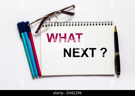 Texte écrit sur le bloc-notes Quoi de suite, concept sur fond blanc.À proximité se trouvent des marqueurs, des lunettes et un stylo. Banque D'Images
