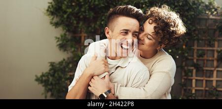 Couple joyeux s'embrassant les uns les autres à l'extérieur.Joyeux jeune couple queer souriant gaiement tout en se tenant ensemble pendant la journée.Jeune couple LGBTQ+ Banque D'Images