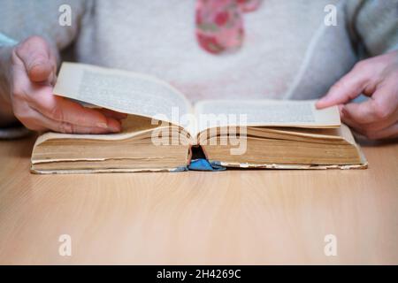 Une femme assise à une table lit et retourne à travers un livre. Mise au point sélective Banque D'Images