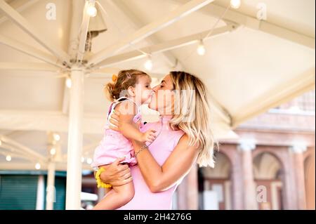 Famille heureuse et aimante - belle mère blonde embrassant et embrassant sa petite fille dans la rue dans le voyage - famille, maternité et concept de personnes Banque D'Images