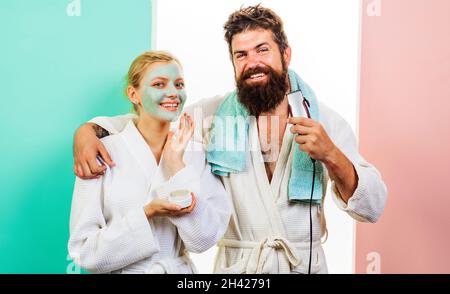 Mari et femme dans la salle de bains.Homme barbu avec rasoir électrique.Femme avec masque facial cosmétique.Procédures matinales.La vie de famille. Banque D'Images