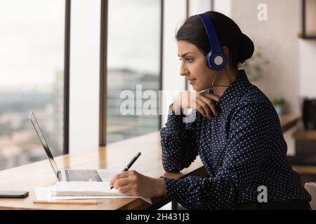Jeune femme indienne concentrée dans les écouteurs étudiant en ligne. Banque D'Images