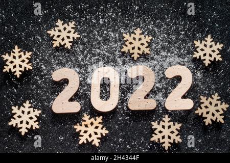 Concept du nouvel an - flocons de neige en bois et numéros 2022 arrosé de neige sur fond étoilé noir étincelant.Carte du nouvel an. Banque D'Images