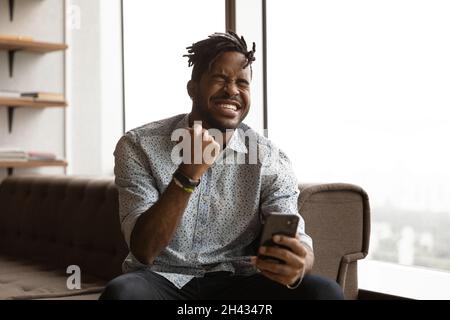 Joyeux jeune homme de race mixte célébrant le succès d'Internet. Banque D'Images