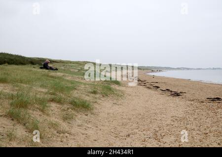 Couple assis et personnes marchant dans le paysage à la plage de Camber Sands en octobre automne Rye Kent Angleterre Kathy DEWITT Banque D'Images
