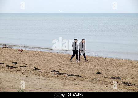 Deux jeunes femmes et chiens marchant le long de la plage à Camber Sands en octobre automne Rye Kent Angleterre Kathy DEWITT Banque D'Images