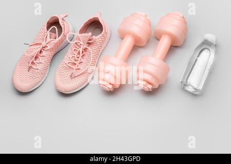 Haltères, chaussures et bouteille d'eau sur fond clair Banque D'Images