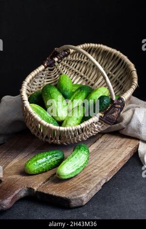 Concombres frais dans un panier en osier sur panneau en bois sur fond noir. Banque D'Images