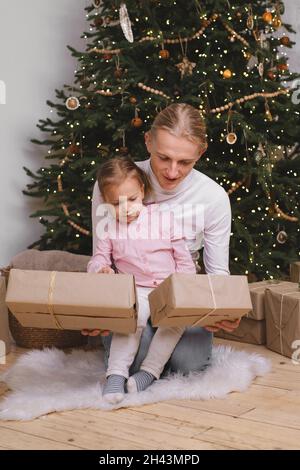 Le père avec l'enfant se prépare pour Noël, emballant les boîtes-cadeaux près de l'arbre.Une famille heureuse rêvant de fêtes et de cadeaux dans un cadre élégant Banque D'Images