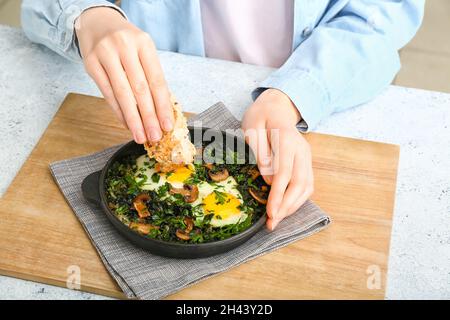 Femme mangeant savoureux Shakshouka à la table de cuisine, en gros plan Banque D'Images