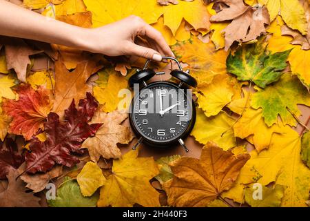 Main féminine avec réveil sur les feuilles d'automne Banque D'Images