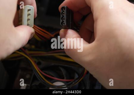 Homme tenant à la main une extrémité mâle et femelle Molex des fiches femelles et les connectant en une seule pièce pour faire fonctionner l'ordinateur à nouveau. Banque D'Images