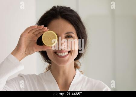 Belle femme tient une tranche de citron, le regard de couverture à l'appareil photo Banque D'Images