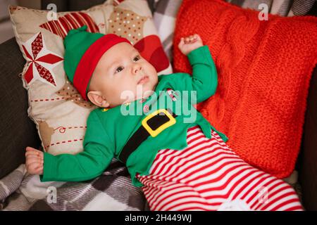 Concept de Noël petit garçon gai elf regarder vers le haut se trouve sur des oreillers multicolores dans le costume de gnome.Le petit assistant du Père Noël Banque D'Images