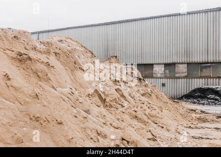 Une grande pile de sable de matériaux industriels naturels est stockée à l'extérieur sur le territoire de l'usine. Banque D'Images