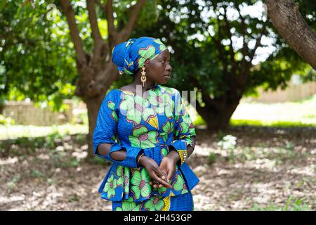 Jolie femme africaine noire dans une élégante robe, debout devant un couple d'arbres attendant quelqu'un Banque D'Images