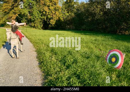 1 une femelle Archer montée sur un cheval arabe blanc avant de tirer une flèche sur Un chemin naturel.Dans le fond Green Meadow et arbres.Grüningen Zurique Banque D'Images