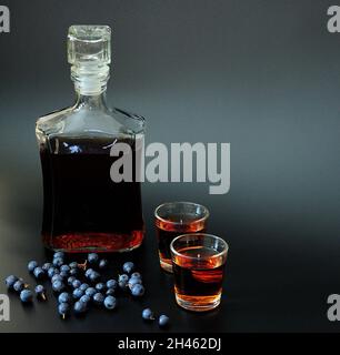 Liqueur de myrtille maison, alcool fort dans deux verres et un carafe en verre sur fond noir, à côté d'une poignée de baies sauvages mûres.Gros plan Banque D'Images